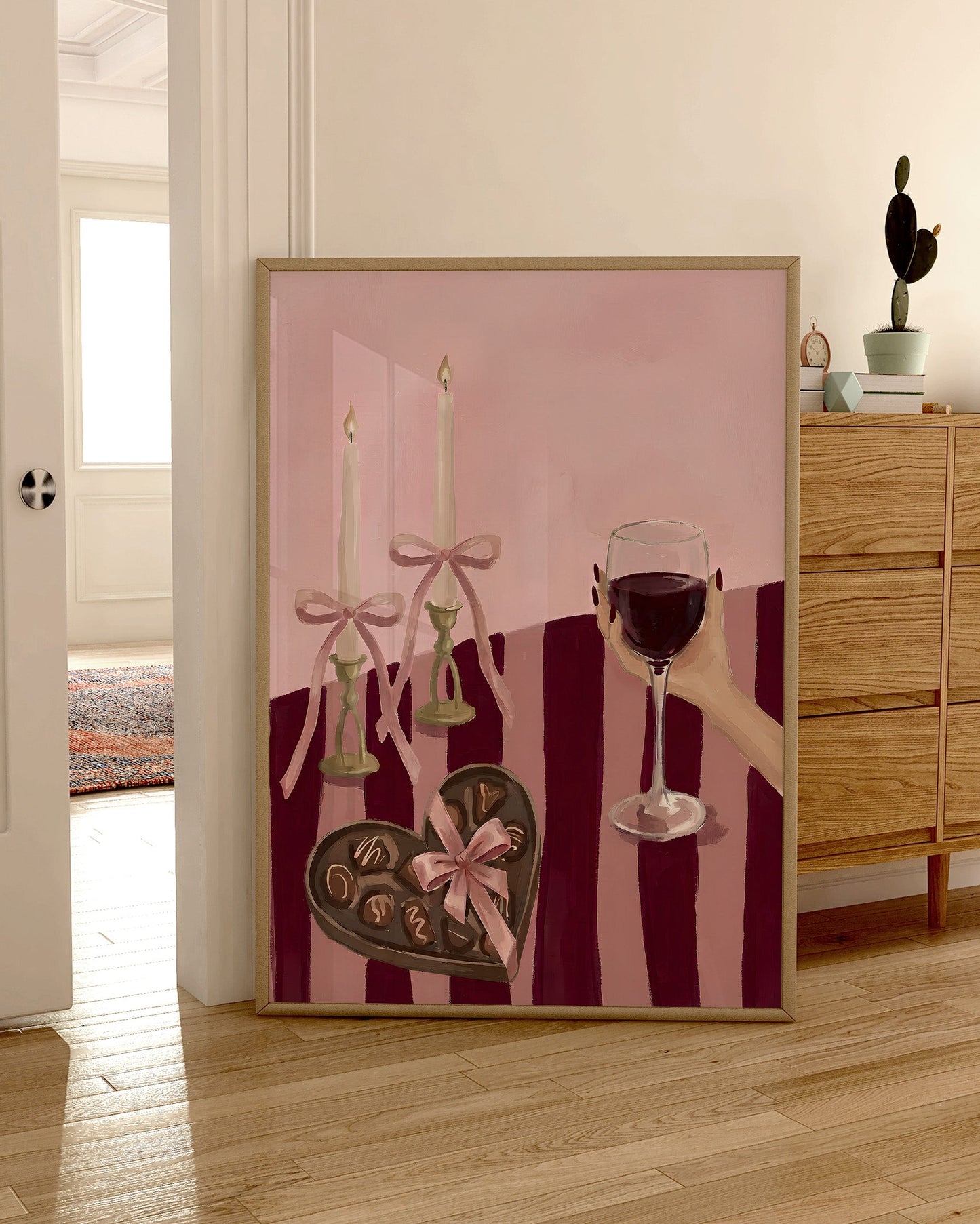 Decorative wall art with a pink background, candles, and a heart-shaped chocolate in a room with wooden furniture.